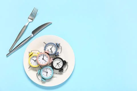 Table setting with alarm clocks on blue background. Intermittent fasting conc Stock Photos