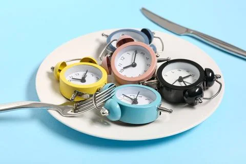 Table setting with alarm clocks on blue background. Intermittent fasting conc Stock Photos