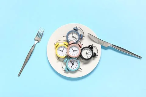 Table setting with alarm clocks on blue background. Intermittent fasting conc Stock Photos