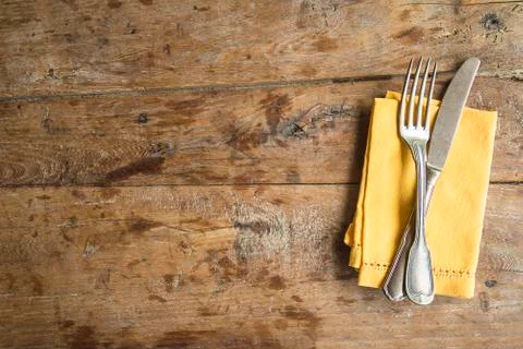 Table setting with antique fork and knife, yellow linen napkin on old wooden  Stock Photos