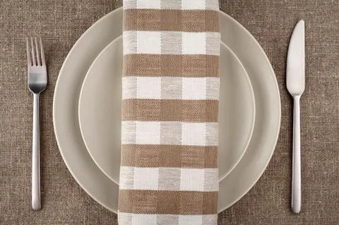 Table setting. Beige plate, fork, knife and beige linen napkin and tablecloth. Stock Photos
