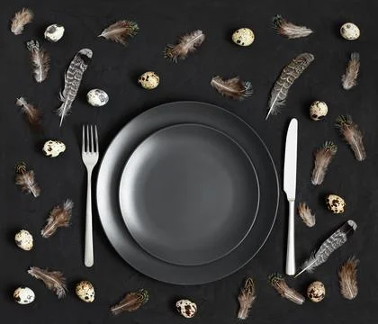 Table setting with a black plate, quail eggs and feathers on a black Stock Photos