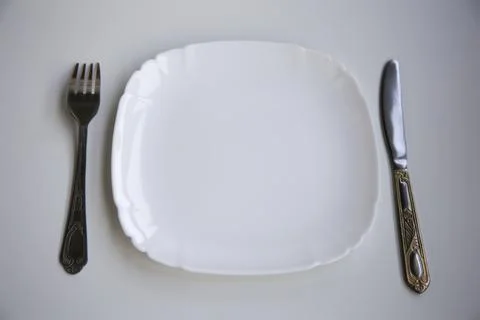 Table setting with a clean white plate, fork and knife laid out on a white ba 库存照片