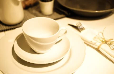 Table setting. Dinner. A white cup stands on two white saucers on a table cov Stock Photos