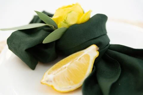 Table setting element lemon slice on a plate, green cloth napkin and yellow f Stock Photos