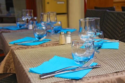 Table setting - knife and fork, glass goblets, blue napkins on beige tableclo Stock Photos
