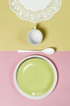 Table setting on a light pink-green background: light green plate, mug, napki Stock Photos