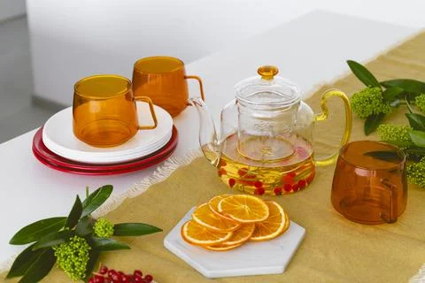 A table setting with orange glass cups, a teapot with tea, fruits and berries Stock Photos