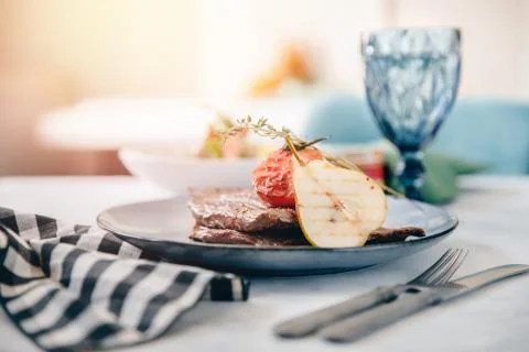 Table setting in restaurant is fresh meat steak with pear and tomato decoration Stock Photos