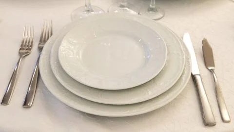 Table setting in a restaurant. Plates, forks and knives on a white tablecloth Stock Photos