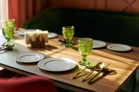 Table setting in the restaurant, white plates, green goblet, wooden table Stock Photos