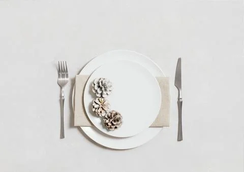 Table setting with silverware, napkin, cones and white plate on white  Stock Photos