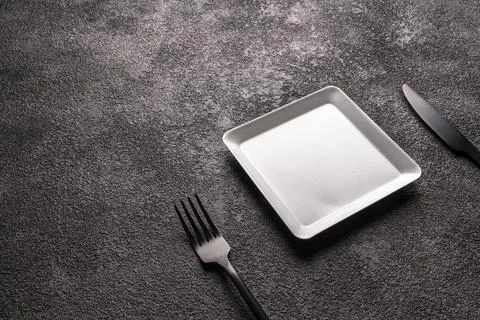 Table setting. A small white square plate and a fork and knife. grey background Stock Photos