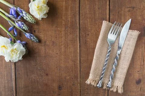 Table setting for spring dinner. Forged fork and knife on burlap napkin, bouq Stock Photos