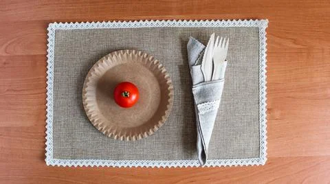 Table setting with a tomato and utensils on a woven placemat in a home kitchen Stock Photos