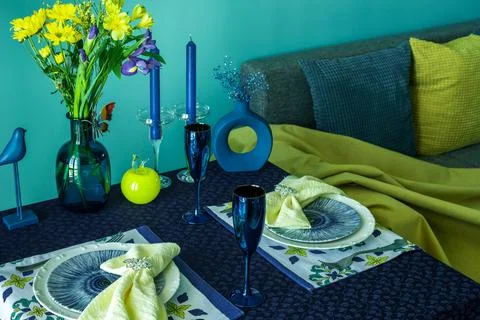 Table setting for two in blue and yellow colors against the background of a sofa Stock Photos