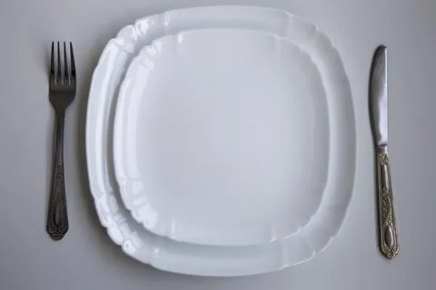 Table setting with two clean white plates and a knife and fork laid out on a Stock Photos
