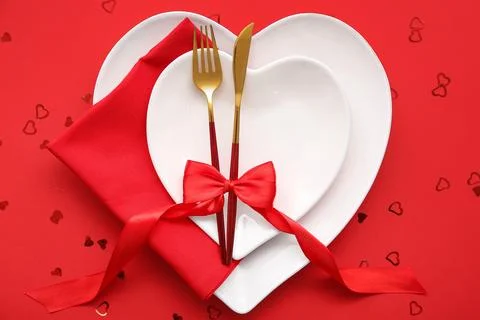 Table setting for Valentine's Day with bow and confetti on red background, cl Stock Photos