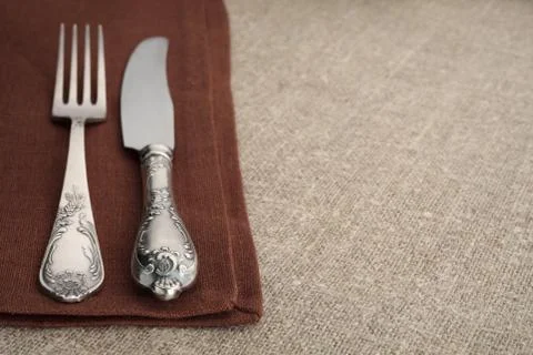 Table setting. Vintage fork and knife on brown napkin with linen tablecloth and Stock Photos