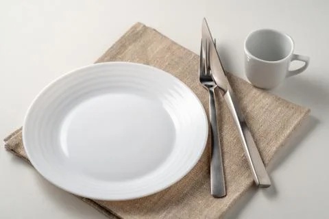 Table setting with a white plate and coffee cup next to cutleries on a white  Stock Photos
