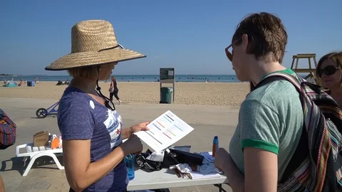 TABLE SIGN-UP PERSON EXPLAINING BEACH CLEAN UP PROCESS TO VOUUNTEERS 스톡 동영상 128333428