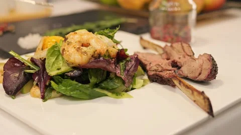 On table sits dish of salad, meat, and shrimp. Indulge in flavors of our Stock Footage 274558930