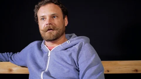 At the table sits a man with a beard and mustache and says something Stock Footage 105840664