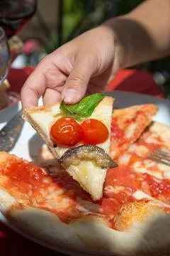 At the table, someone picks up a slice of pizza with tomatoes and basil. Round Stock Photos