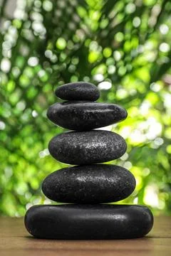 Table with stack of stones and blurred green leaves on background. Zen concep Stock Photos