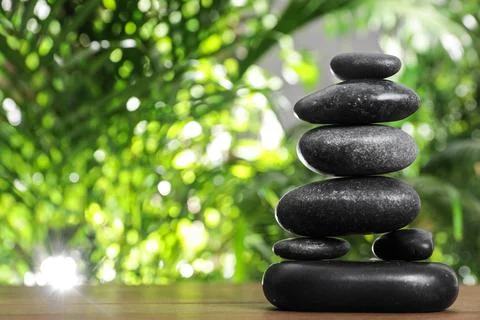 Table with stack of stones and blurred green leaves on background, space for  库存照片