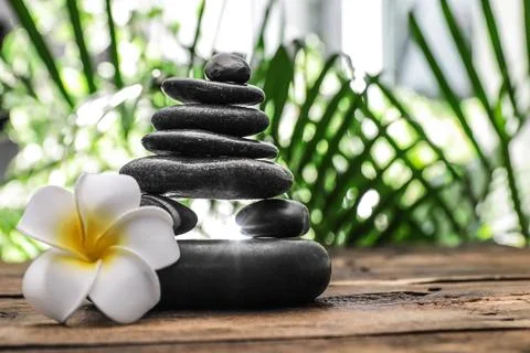 Table with stack of stones, flower and blurred green leaves on background, sp Foto stock