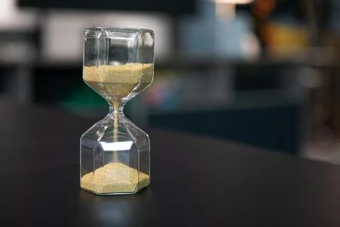 On a table stand an egg timer made of glass, which is filled with small balls Stock-Fotos