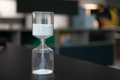On a table stand an egg timer made of glass, which is filled with small balls Stock-Fotos