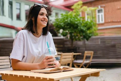 Table of a summer cafe sits a pretty girl with a smile watching passers-by with Stock-Fotos