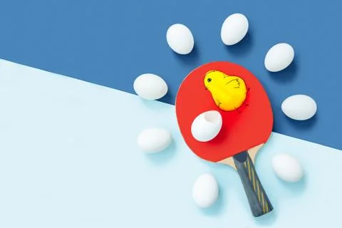 A table tennis racket is lying on table. There are identical eggs around racket Stock Photos