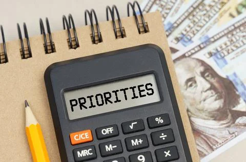 On the table there are dollars, a notebook and a calculator with the inscript Stock Photos