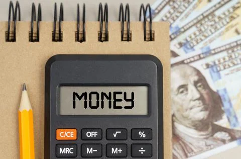 On the table there are dollars, a notebook and a calculator with the inscript Stock Photos