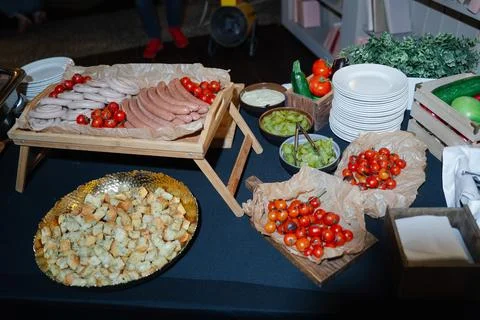 On the table there are prepared plates and trays with sausages, vegetable Stock Photos