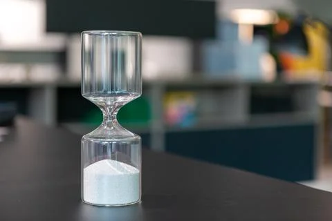 On  table there is a glass egg timer filled with small balls Stock Photos
