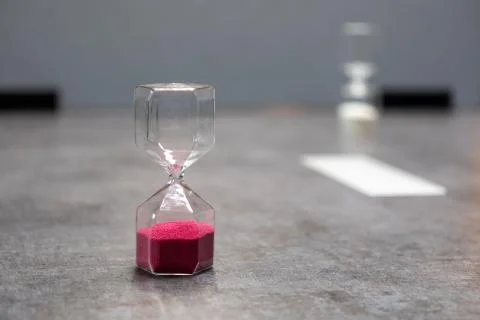 On  table there is a glass egg timer filled with small balls Stock Photos