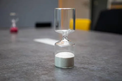 On a table there is a glass egg timer filled with small balls 스톡 사진