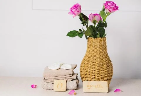On the table there is one stack of baby clothes with a wicker vase and roses. Stockfoto's