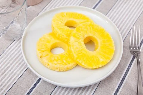 On table there is plate with summer dessert - round pieces of pineapple pulp. Stock Photos