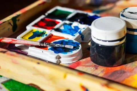 On a table, there is a tray filled with vibrant watercolors and a brush Stock Photos