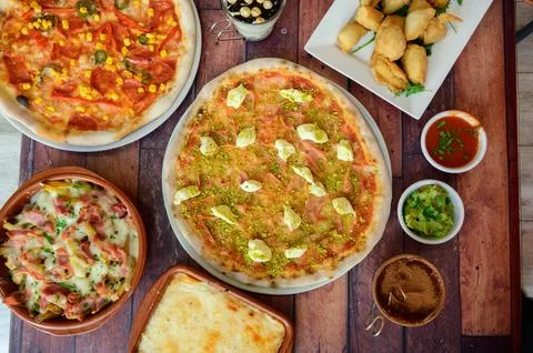 A table with three different pizzas and a variety of side dishes Stock Photos