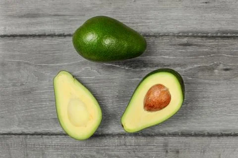 Table top view on avocado cut in half, with whole one above, placed on wood d Stock Photos