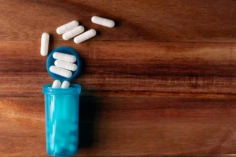 A table top view of blue pill bottle with white pills inside Stock Photos