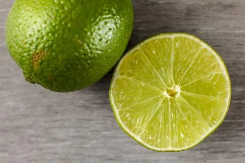 Table top view on green lime cut in half and part of whole one, on a gray woo Stock Photos