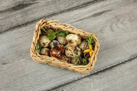 Table top view - square basket with quail eggs and some green leaves placed o Stock Photos