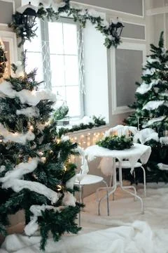 Table with two chairs between Christmas trees covered with snow and garlands  Stock Photos